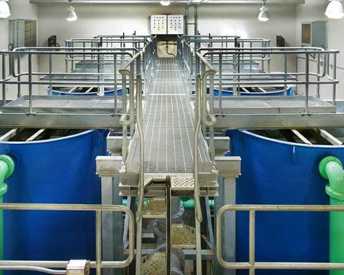 Aluminum grating walkways above six large blue tanks with green piping at the Indian Head Wastewater Treatment Plant.