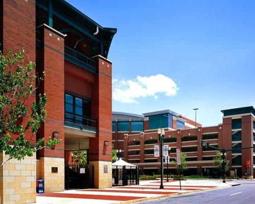 Exterior photo of Jacksonville Municipal Garages. Photo is a view from the street of the sports arena parking garage. Trees line the street. Red brick with green trim accent the garage.