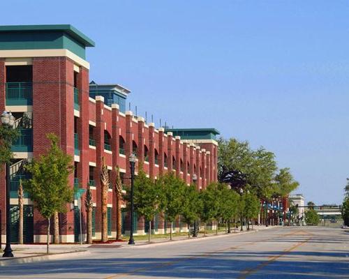 Exterior photo of Jacksonville Municipal Garages. Photo is a streetscape view of the parking garage with a church steeple in the background. Trees line the street. Red brick with green trim accent the garage.