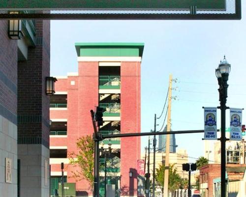 Exterior photo of Jacksonville Municipal Garages. Photo is through a doorway outside the arena. Trees line the street. Red brick with green trim accent the garage. Sign above doorway reads 'Exit Home Plate Gate'.