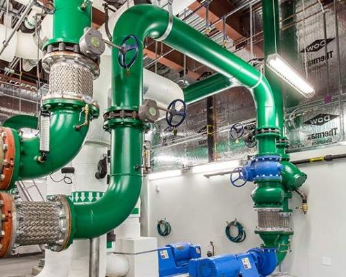 Photo from inside the central energy plant with green piping and blue pumps.